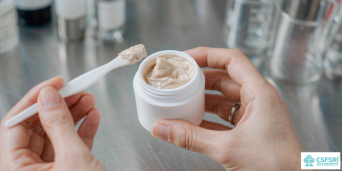 A formulators hands holding a small white cream jar with a tiny spatula in a clean laboratory