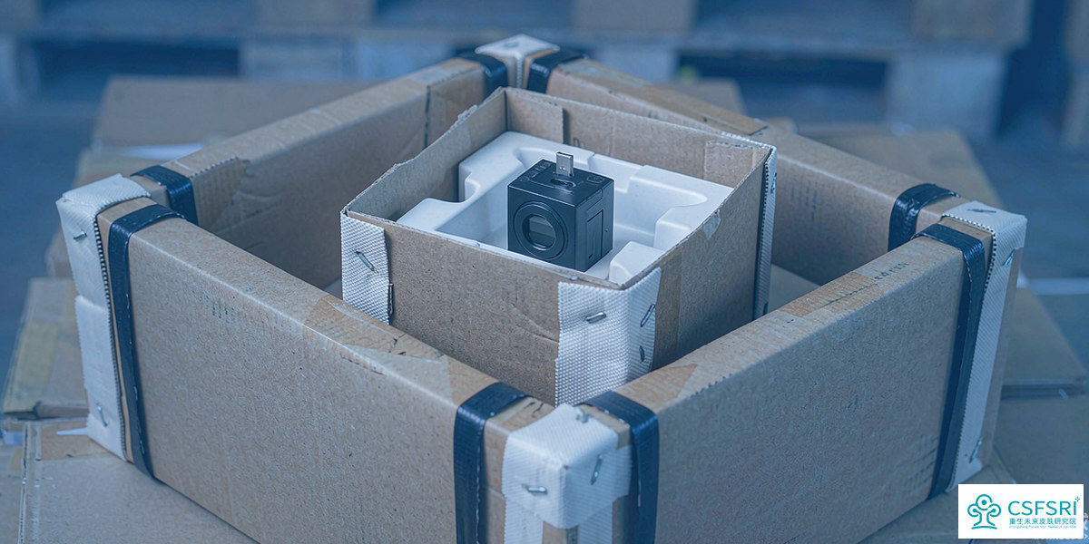 Stack of cosmetic shipping cartons on a warehouse pallet, a USB temperature data logger resting on top of one open carton, soft industrial light